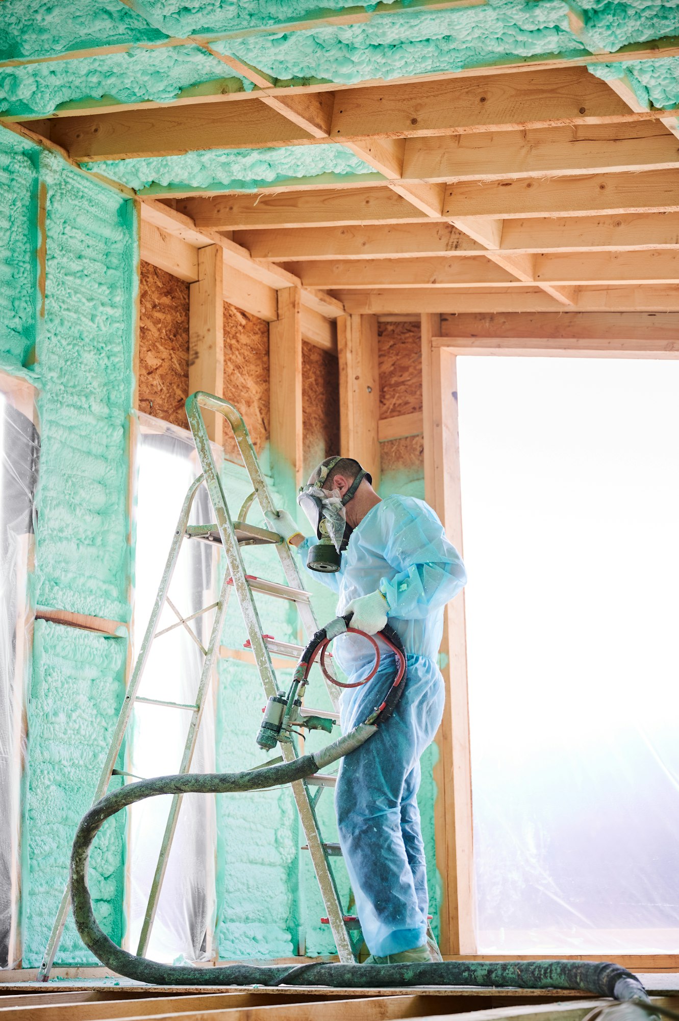 Worker spraying polyurethane foam for insulating wooden frame house.